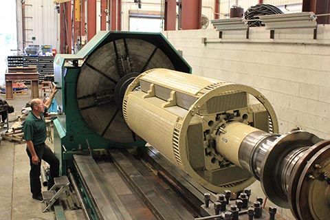 A large electric motor's rotor is on an industrial lathe machine.