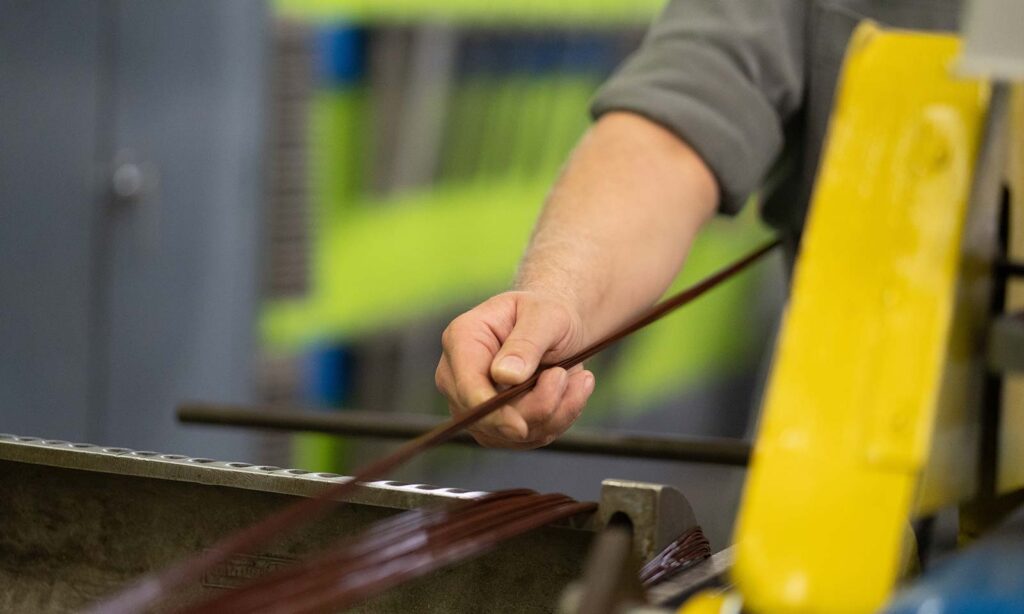 Skilled hands carefully pulling a copper coil with precision.