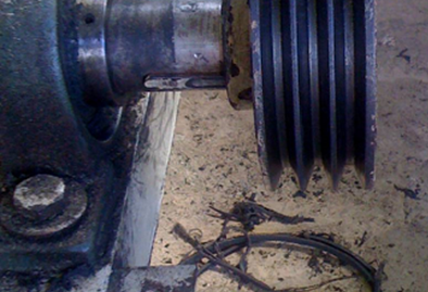 Misaligned motor with a shredded belt laying on the shop floor next to a motor.